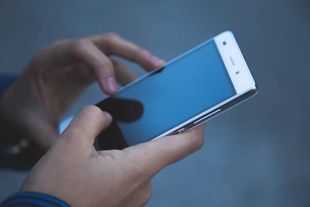 An adult pair of hands holds a smartphone with the phone screen facing outward.