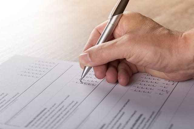 Close-up image of an adult hand holding a silver and black pen, poised over lined paper.